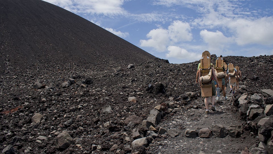  A group of tourists climbing the Volcano Cerro Negro with their boards on the way to volcano board back down it.